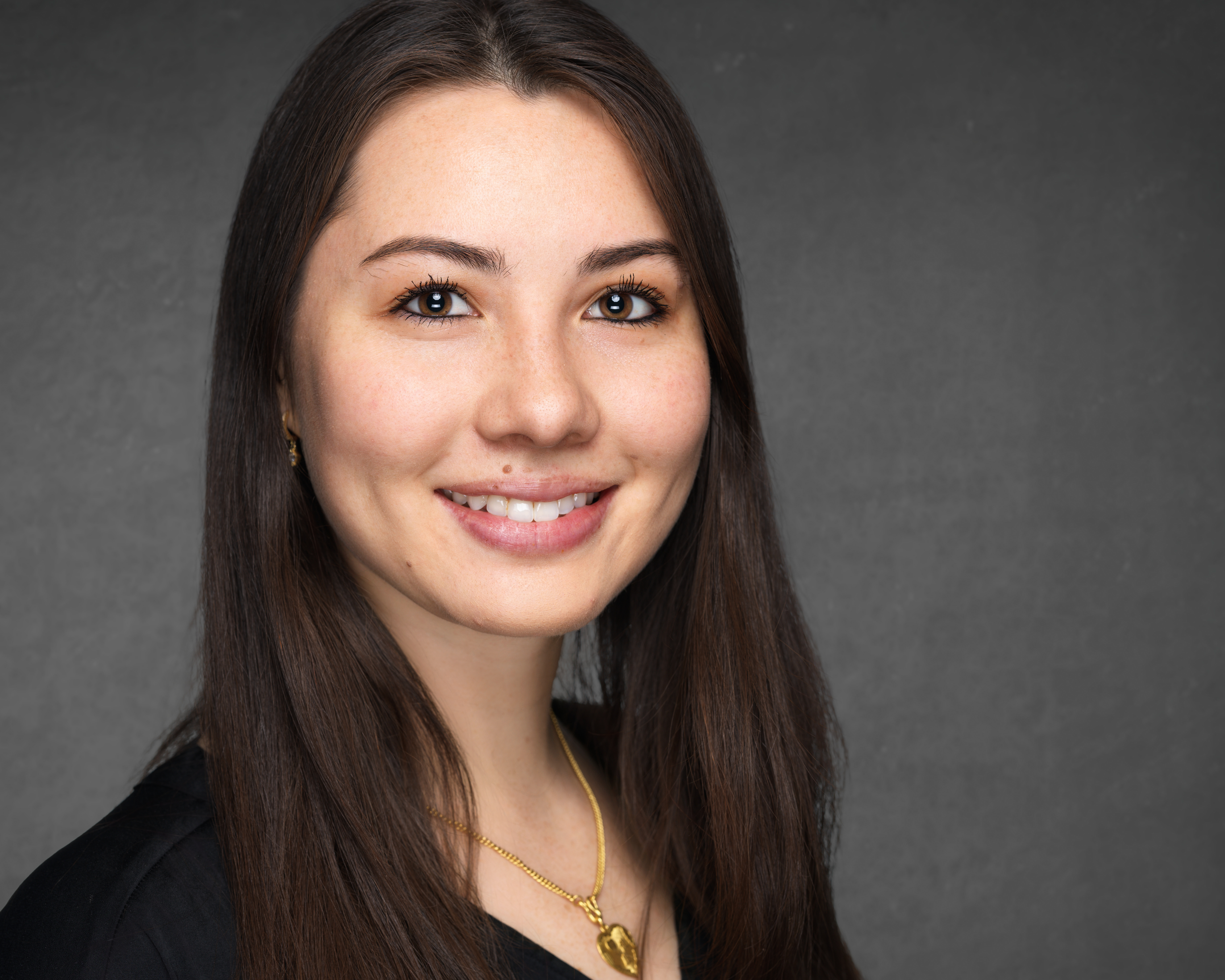 Woman with brown hair in a black shirt smiling against a gray background