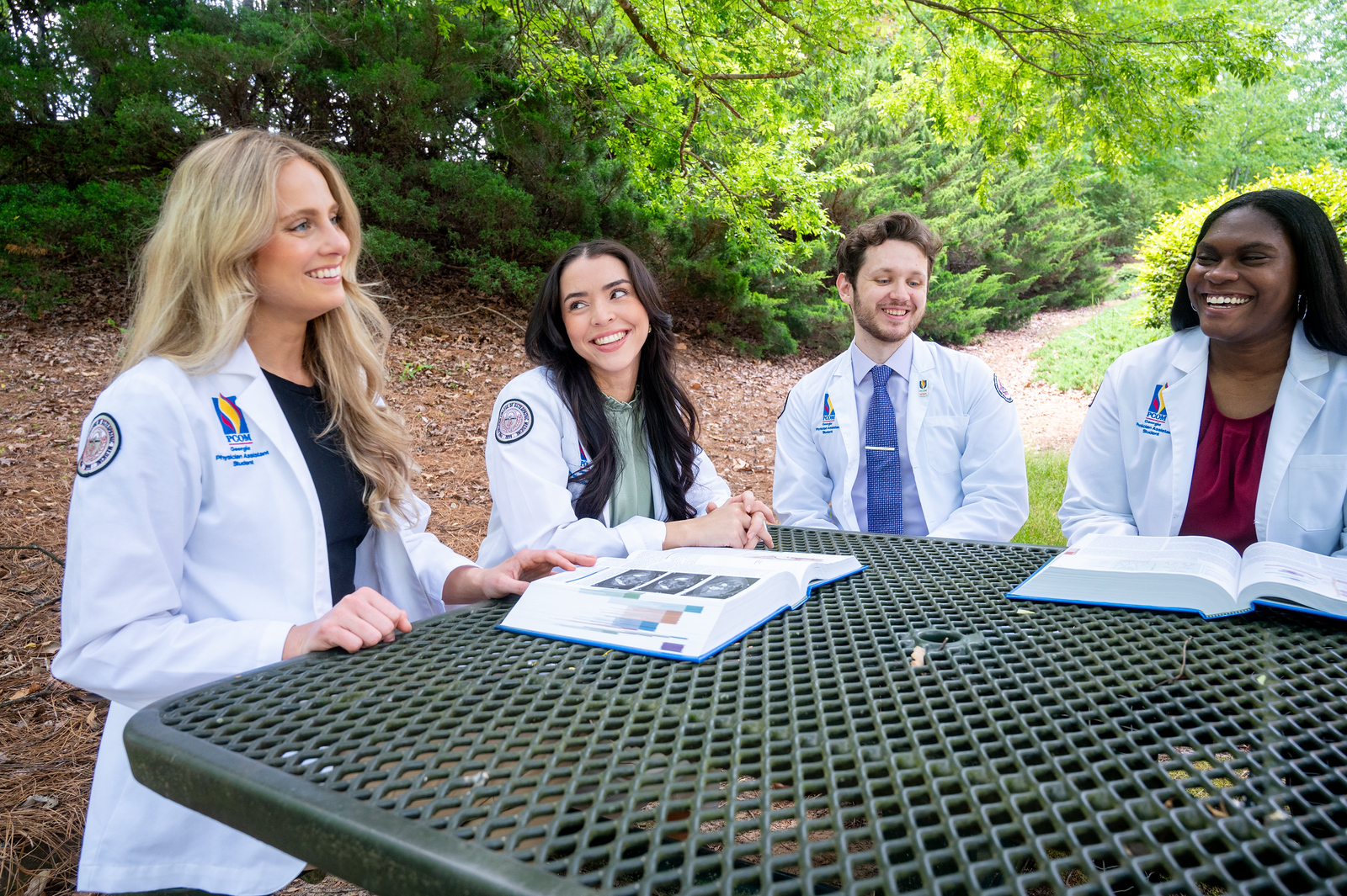 Four students gathered around a table outside to study in their white coats.