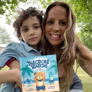 Gina DeGregorio-Sonbert smiles while hugging her son and holding her book, Theodore Bearkins, outside under a tree